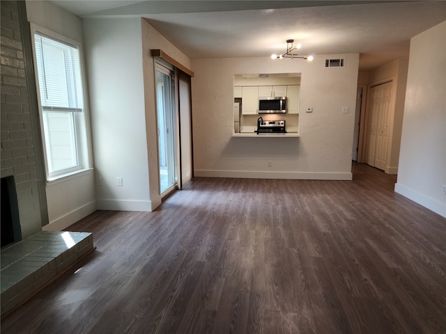 unfurnished living room featuring a fireplace, dark wood-type flooring, plenty of natural light, and an inviting chandelier