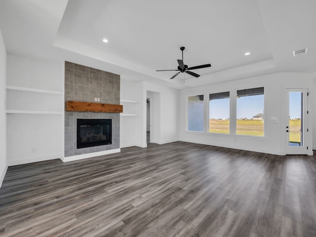 unfurnished living room with built in shelves, dark hardwood / wood-style floors, a tray ceiling, ceiling fan, and a tiled fireplace