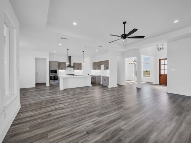 unfurnished living room with dark hardwood / wood-style floors, a tray ceiling, ceiling fan with notable chandelier, and sink