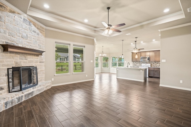 unfurnished living room featuring ceiling fan with notable chandelier, dark hardwood / wood-style flooring, sink, a stone fireplace, and a raised ceiling