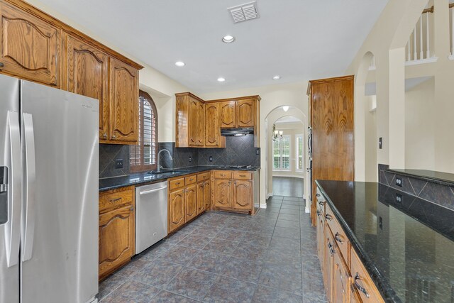 kitchen with appliances with stainless steel finishes, tasteful backsplash, dark tile patterned flooring, and dark stone countertops