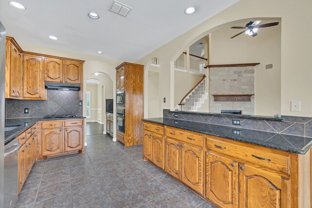 kitchen with dark stone countertops, decorative backsplash, appliances with stainless steel finishes, ceiling fan, and dark tile patterned flooring