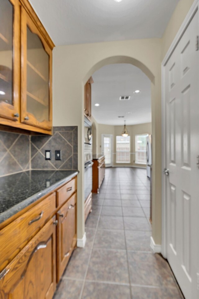 kitchen with light tile patterned flooring, fridge, decorative light fixtures, and backsplash