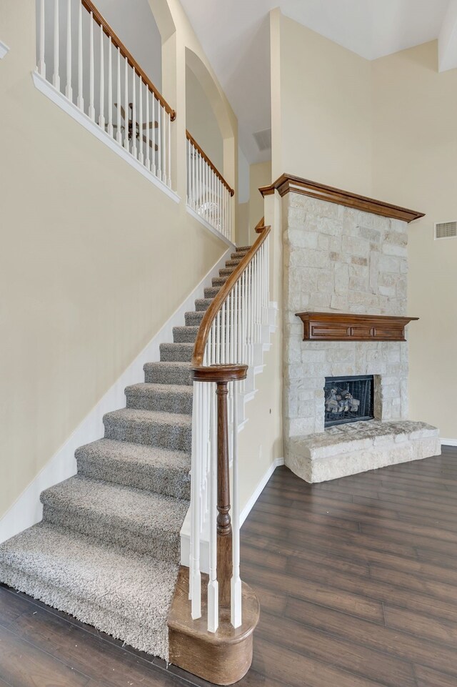 stairway featuring wood-type flooring, a fireplace, and a towering ceiling