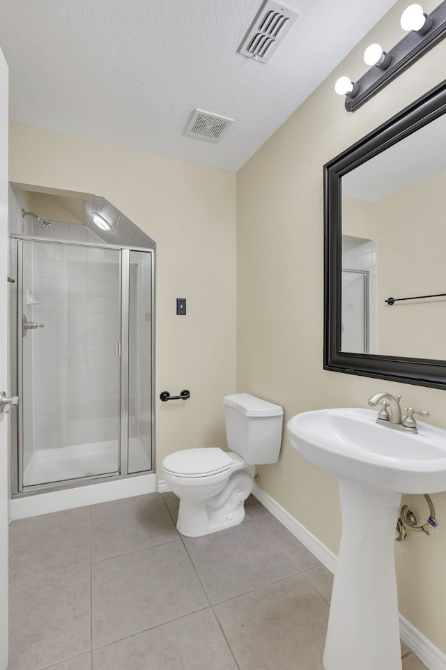 bathroom with a textured ceiling, toilet, tile patterned floors, and a shower with shower door