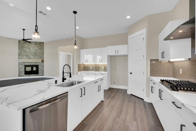 kitchen featuring pendant lighting, white cabinetry, sink, stainless steel appliances, and wall chimney range hood