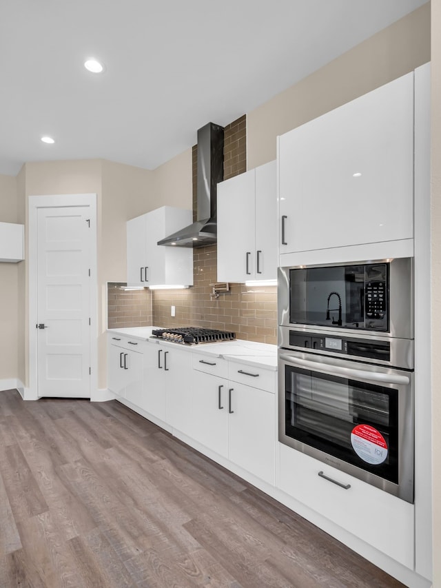 kitchen featuring stainless steel gas stovetop, white cabinetry, backsplash, wall chimney exhaust hood, and light hardwood / wood-style flooring