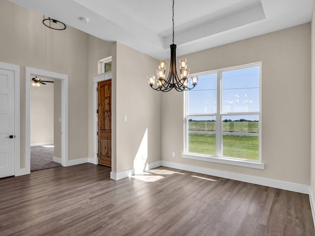 unfurnished dining area featuring dark hardwood / wood-style floors, a raised ceiling, and a notable chandelier