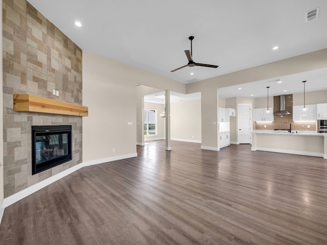 unfurnished living room featuring ceiling fan, dark hardwood / wood-style floors, a tiled fireplace, and sink