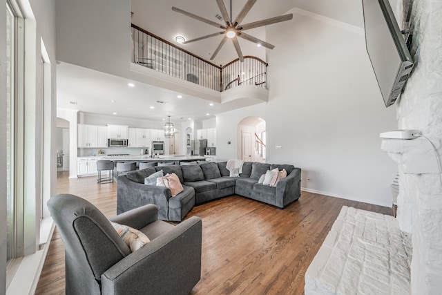 living room with ceiling fan, light hardwood / wood-style flooring, a towering ceiling, crown molding, and a premium fireplace