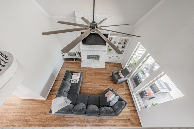 interior space with ceiling fan, hardwood / wood-style floors, a stone fireplace, and ornamental molding