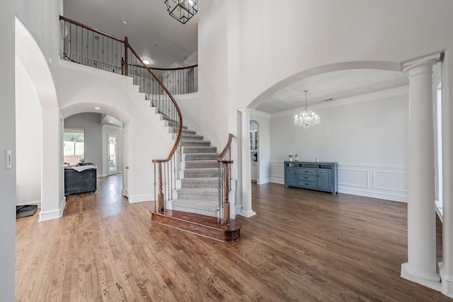 foyer entrance with hardwood / wood-style floors, a towering ceiling, decorative columns, an inviting chandelier, and crown molding