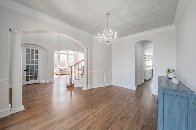 spare room with a notable chandelier, crown molding, hardwood / wood-style floors, and ornate columns