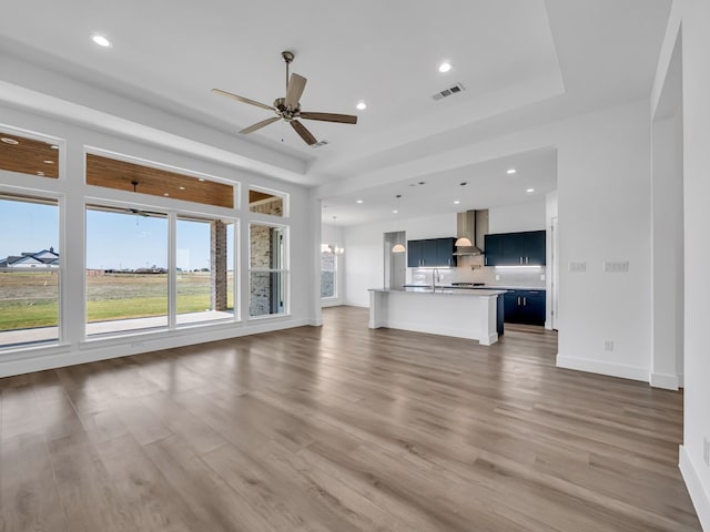 unfurnished living room featuring dark hardwood / wood-style floors, sink, a tray ceiling, and ceiling fan with notable chandelier