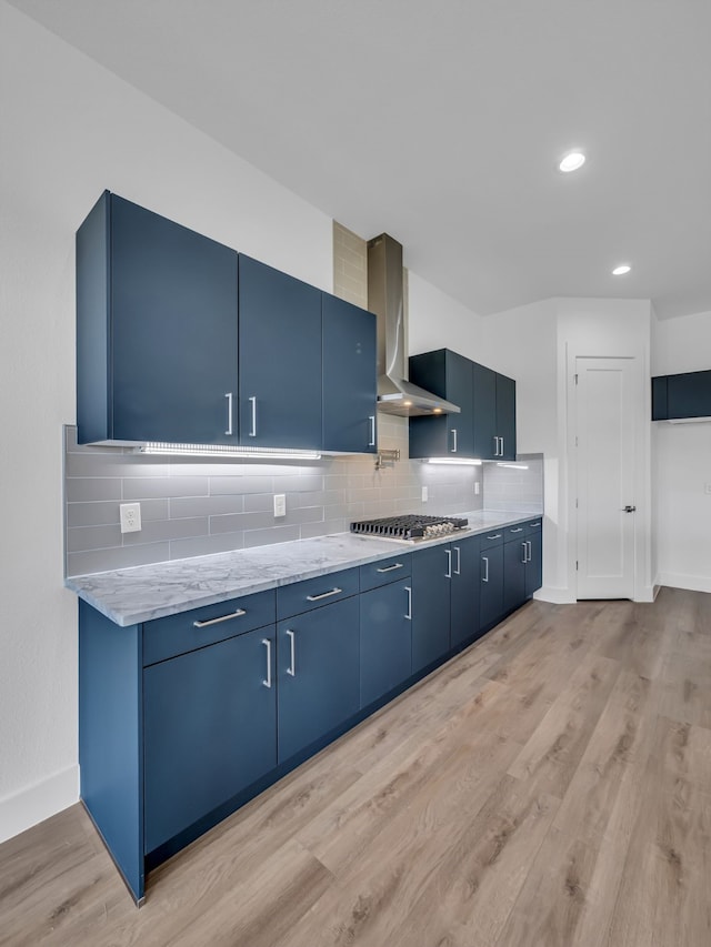 kitchen featuring tasteful backsplash, wall chimney range hood, blue cabinetry, and light wood-type flooring