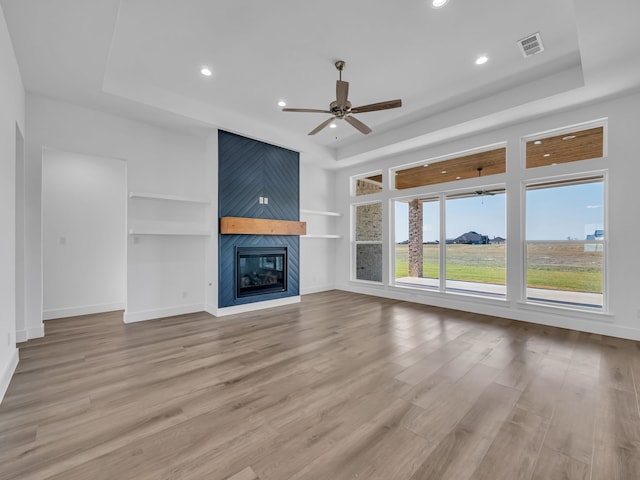 unfurnished living room with a fireplace, a raised ceiling, built in features, and light hardwood / wood-style flooring