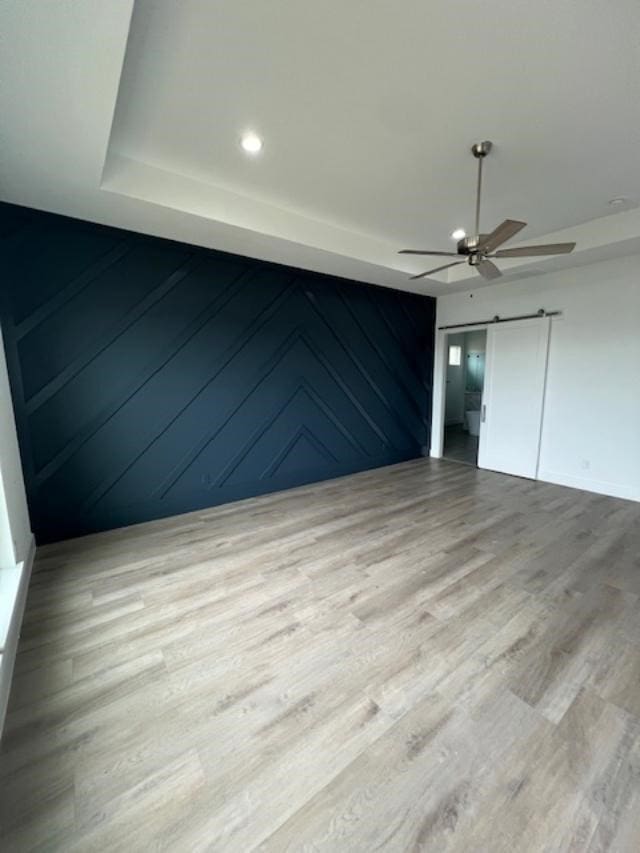 unfurnished room featuring a barn door, ceiling fan, and light wood-type flooring