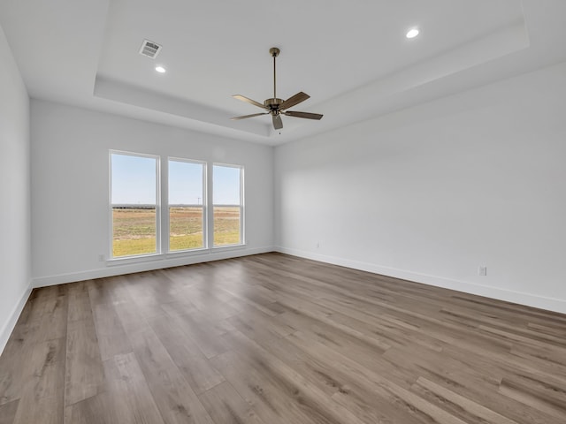 spare room with a raised ceiling, ceiling fan, and light wood-type flooring