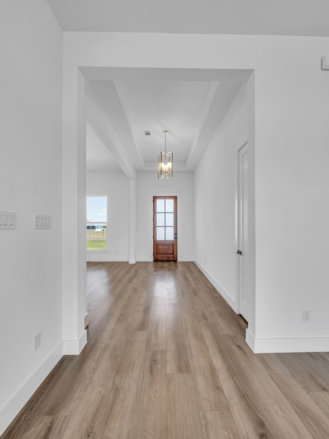 foyer entrance featuring an inviting chandelier, light hardwood / wood-style floors, and a raised ceiling