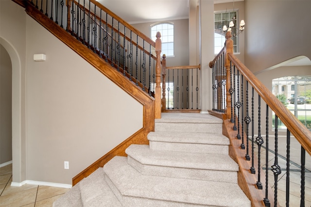 staircase with tile patterned floors, ornamental molding, a high ceiling, and a healthy amount of sunlight