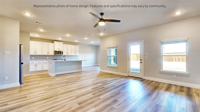 kitchen with stainless steel appliances, a kitchen island with sink, white cabinets, ceiling fan, and light hardwood / wood-style flooring