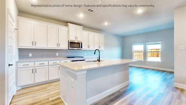 kitchen featuring decorative backsplash, white cabinetry, light hardwood / wood-style floors, an island with sink, and sink