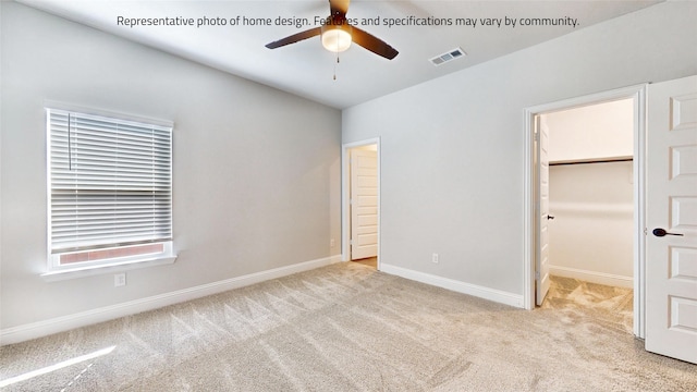 unfurnished bedroom featuring ceiling fan, a walk in closet, a closet, and light colored carpet