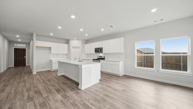 kitchen with sink, stainless steel appliances, an island with sink, white cabinets, and light wood-type flooring