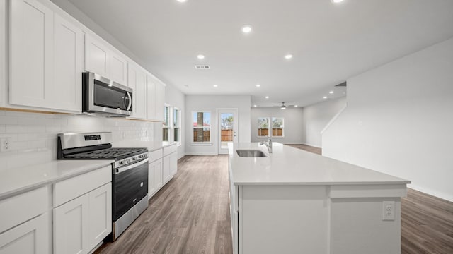 kitchen with appliances with stainless steel finishes, a kitchen island with sink, and white cabinets