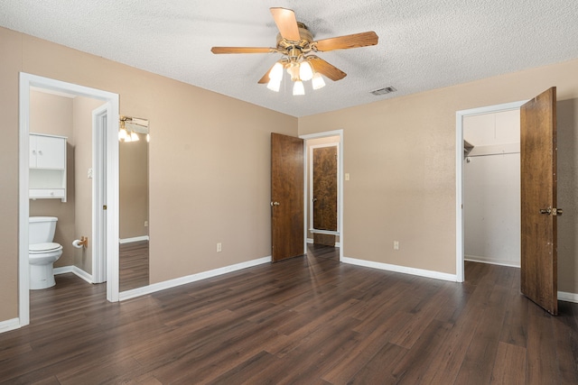 unfurnished bedroom featuring dark wood-type flooring, a walk in closet, a closet, and ceiling fan