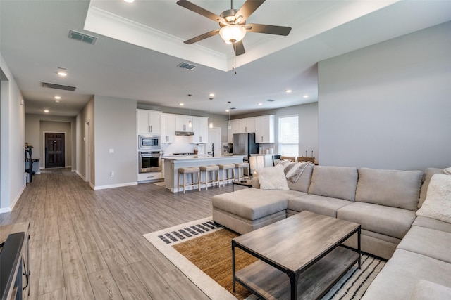 living room with light wood-style floors, baseboards, visible vents, and a raised ceiling