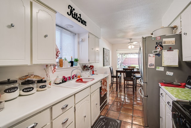 kitchen with a textured ceiling, ceiling fan, sink, white cabinets, and dark tile patterned flooring