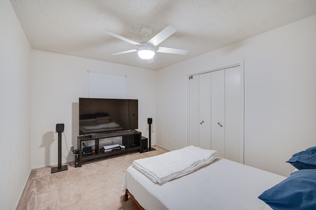 bedroom with ceiling fan, a textured ceiling, light carpet, and a closet