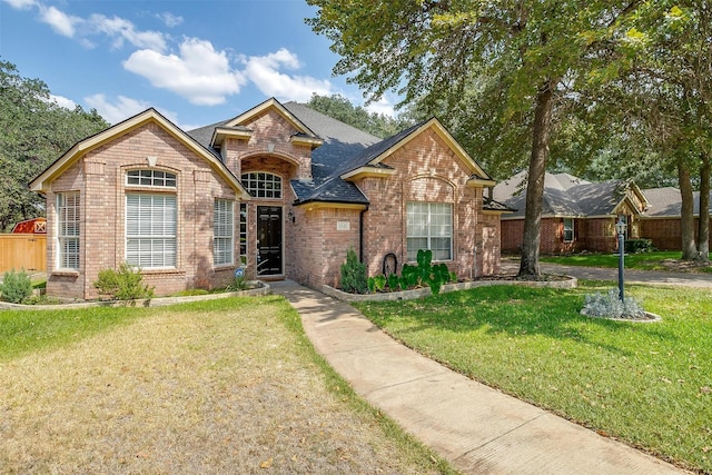 traditional home featuring roof with shingles, a front lawn, and brick siding