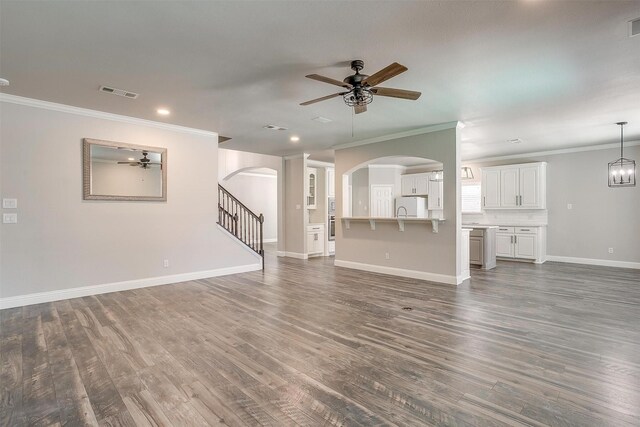 unfurnished living room featuring ceiling fan with notable chandelier, dark wood-type flooring, and crown molding