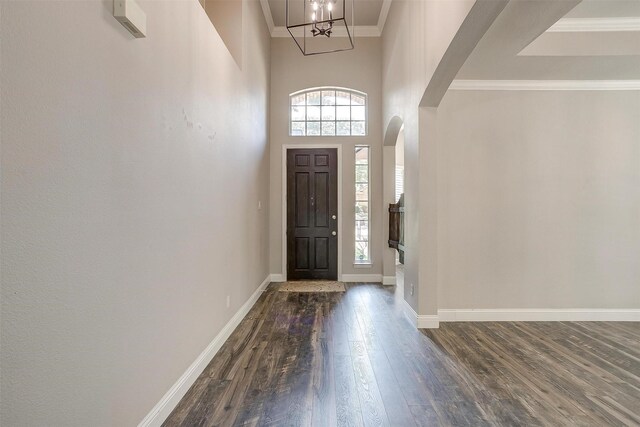 entrance foyer featuring a towering ceiling, dark wood-type flooring, a wealth of natural light, and a notable chandelier