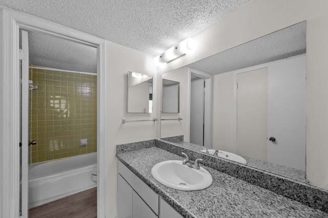 full bathroom with a textured ceiling, toilet, hardwood / wood-style floors, tiled shower / bath combo, and vanity