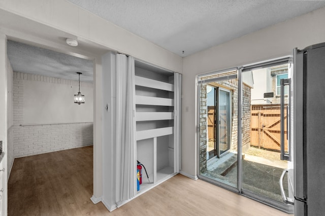 interior space with light hardwood / wood-style flooring, a textured ceiling, and brick wall