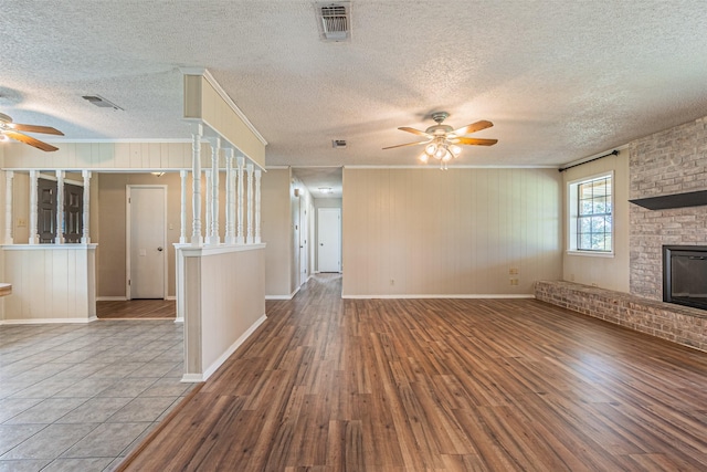 unfurnished living room with wood-type flooring, a brick fireplace, ornamental molding, and ceiling fan