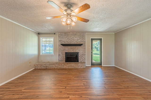 unfurnished living room with ceiling fan, ornamental molding, wood-type flooring, and a brick fireplace