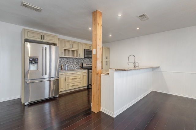 kitchen with dark wood-type flooring, light stone counters, stainless steel appliances, cream cabinets, and decorative backsplash