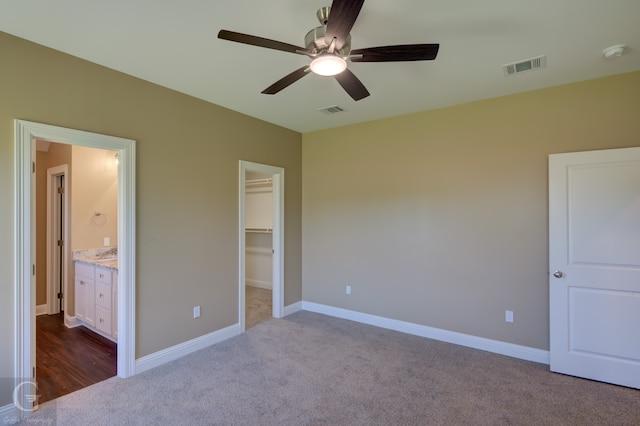 unfurnished bedroom with carpet flooring, ceiling fan, a closet, connected bathroom, and a walk in closet