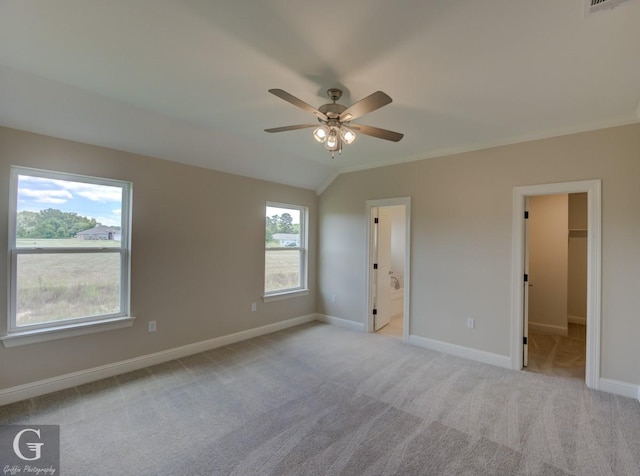 unfurnished bedroom with lofted ceiling, ceiling fan, ensuite bathroom, a walk in closet, and light colored carpet