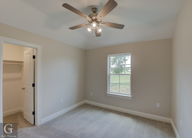 unfurnished bedroom featuring light carpet, a spacious closet, ceiling fan, and a closet