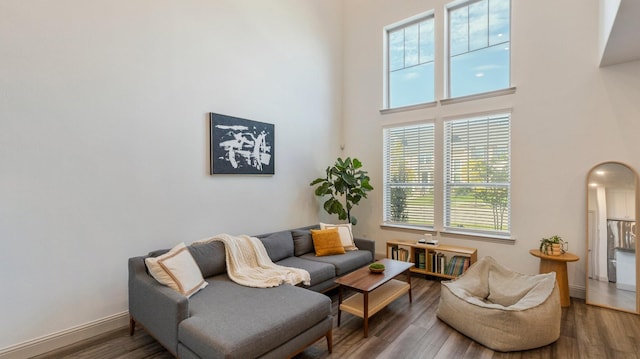 living area with dark wood-style floors, arched walkways, a towering ceiling, and baseboards