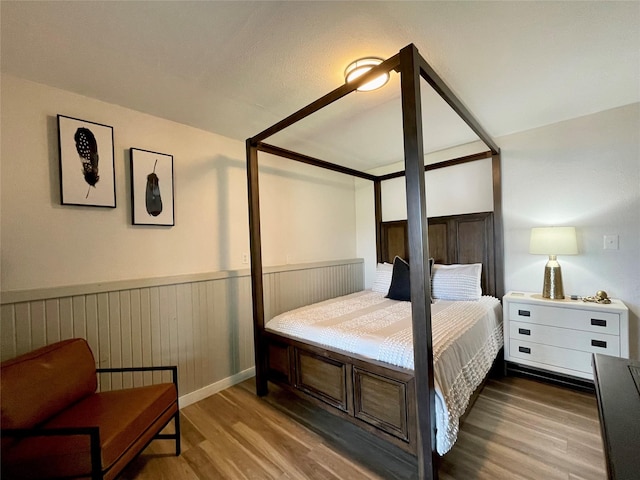 bedroom with a wainscoted wall and wood finished floors