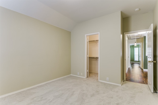 unfurnished bedroom featuring vaulted ceiling, a walk in closet, light carpet, and a closet