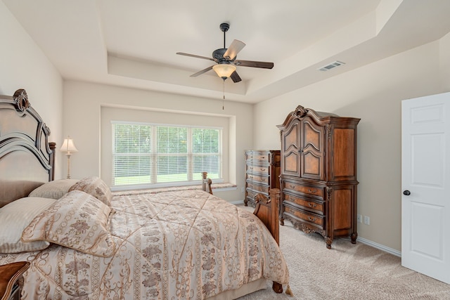 carpeted bedroom with ceiling fan and a tray ceiling