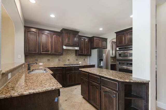 kitchen with sink, decorative backsplash, appliances with stainless steel finishes, dark brown cabinets, and kitchen peninsula