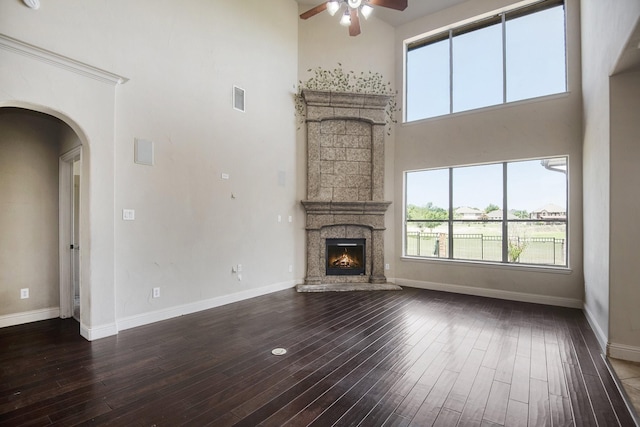 unfurnished living room featuring a high ceiling, dark hardwood / wood-style flooring, a large fireplace, and ceiling fan